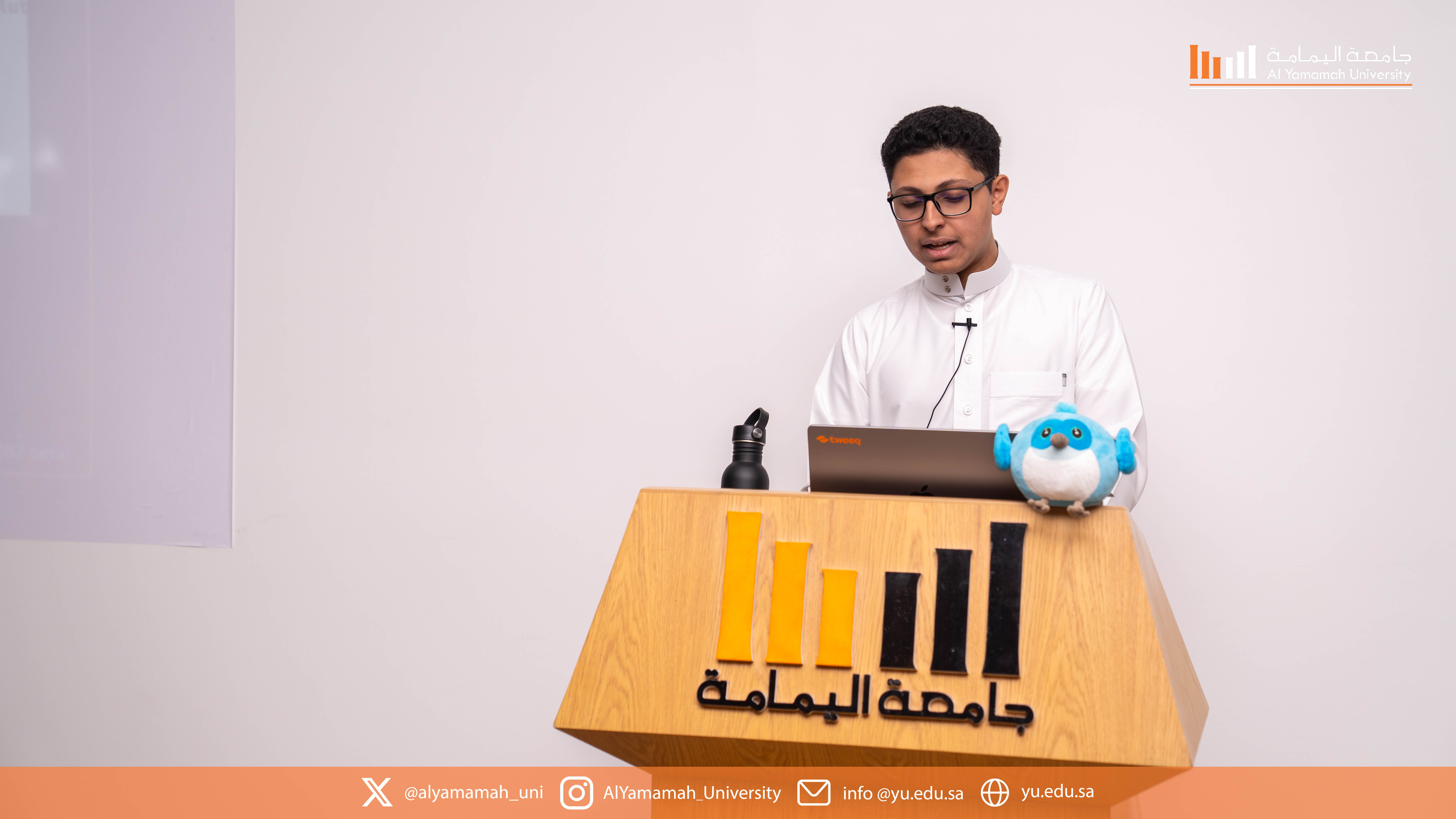 Yazeed AlKhalaf presenting the Flutter workshop with the Flutter mascot on the podium